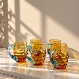 May include: A set of four amber-colored glass mugs featuring a dimpled, textured surface and a distinct, curved handle in a translucent teal blue color. Each mug has a rounded body and a smooth rim, showcasing a vibrant contrast between the warm yellow-orange glass and the cool blue accents.
