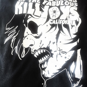 May include: Black t-shirt with a white graphic of a stylized, monstrous face with sharp teeth and dripping saliva. The text "THE TRUE LIVES OF THE FABULOUS KILLJOYS CALIFORNIA" is printed above the face. The design includes a spider symbol.