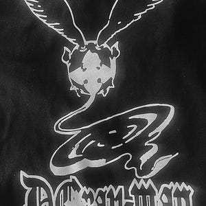 May include: Black graphic tee featuring a white design of a winged creature above stylized text. The text includes the words "D.Gray-man" and Japanese characters. The design is centered on the shirt.