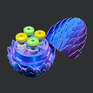 May include: A blue and purple 3D-printed dragon egg container, open to reveal four small glass vials with yellow and green lids. The egg's exterior features a scale-like design. The container is on a dark background.