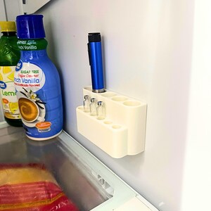 Insulin pen and peptide vial fridge organizer mounted inside refrigerator wall, GLP-1 storage holder keeping injection pens and cartridges visible, clean and discreet cold storage organization system