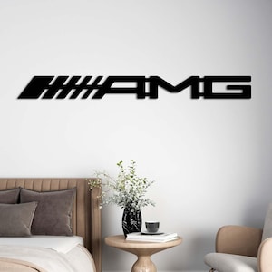 May include: Black metal AMG logo wall art. The logo is displayed horizontally on a white wall above a bed. The room also features a side table, chair, and curtains.