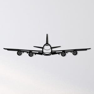 以下が含まれることがあります： 黒い金属製の飛行機のウォールアート。飛行機は正面から見た図で、胴体、翼、尾翼、4つのエンジンが描かれています。デザインはミニマリストでモダンで、航空愛好家に適しています。