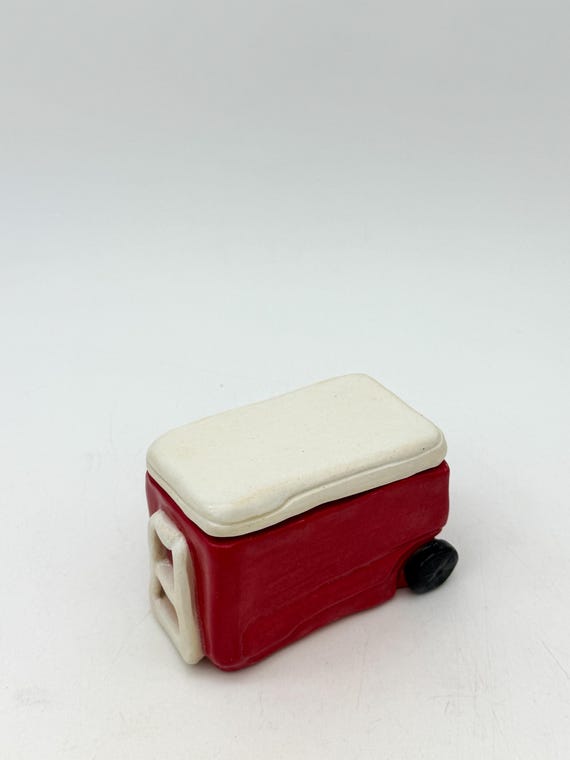 A tiny ceramic beach cooler that opens up as a trinket box — the retro summertime miniature detail makes it a genuinely delightful desk or shelf object.
