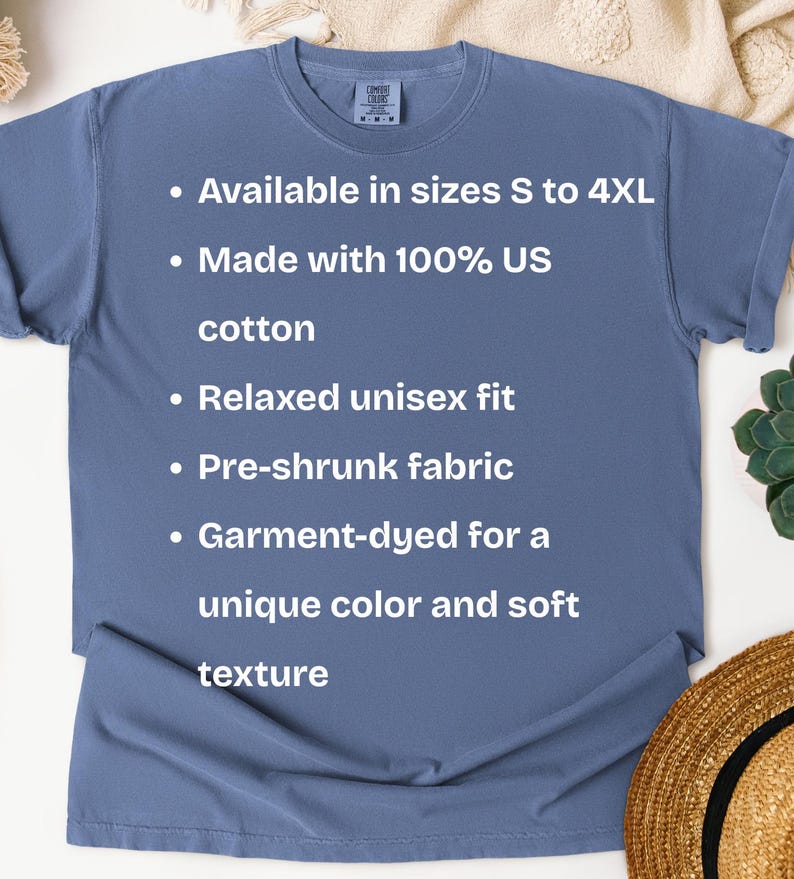K&ouml;nnte beinhalten: Ein staubblaues T-Shirt mit dem Text: "Erh&auml;ltlich in den Gr&ouml;&szlig;en S bis 4XL, Hergestellt aus 100 % US-Baumwolle, Entspannte Unisex-Passform, Vorgeschrumpfter Stoff, Kleidungsst&uuml;ckgef&auml;rbt f&uuml;r eine einzigartige Farbe und weiche Textur."