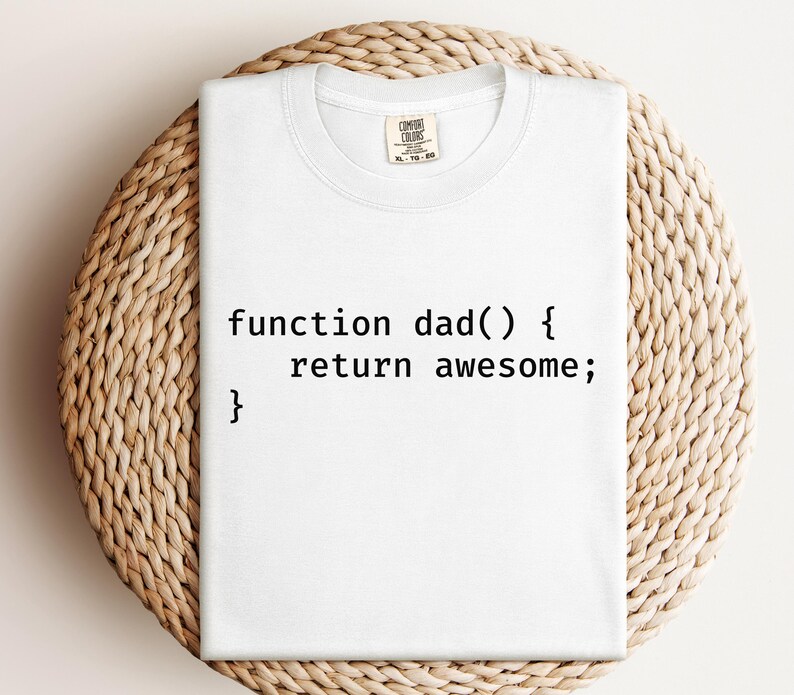 K&ouml;nnte beinhalten: Wei&szlig;es T-Shirt mit dem Text "function dad() { return awesome; }" in Schwarz, ein humorvolles Design im Coding-Stil. Das Shirt ist von der Marke Comfort Colors und wird auf einer hellbraunen, gewebten Oberfl&auml;che pr&auml;sentiert.