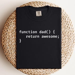 K&ouml;nnte beinhalten: Schwarzes T-Shirt mit dem wei&szlig;en Text "function dad() { return awesome; }". Das gefaltete T-Shirt liegt auf einer runden, gewebten Matte. Das Shirt hat einen Rundhalsausschnitt und kurze &Auml;rmel.