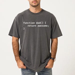 May include: Dark gray t-shirt with the text "function dad() { return awesome; }" in white. The shirt is a crew neck style and has short sleeves. The fabric appears to be a soft, worn material.