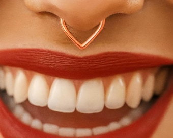 Könnte beinhalten: Nahaufnahme eines Gesichts mit einem kupferfarbenen Septumring in V-Form. Der Text "NO PIERCING NEEDED" befindet sich über der Nase. Die Person lächelt und zeigt weiße Zähne und roten Lippenstift.