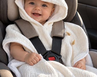 May include: A cream-colored hooded poncho made of textured muslin fabric. The garment features a loose, draped fit with a hood that covers the head and wide openings for the arms, providing a soft, lightweight layer over the shoulders.