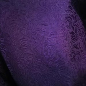 May include: Purple fabric with a textured, floral pattern. The fabric has a subtle sheen and a soft, luxurious feel.