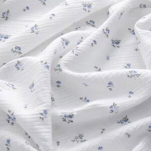 Peut inclure: Tissu en coton blanc avec un petit imprim&eacute; floral bleu. Le tissu a une surface textur&eacute;e, semblable &agrave; une gaufre.