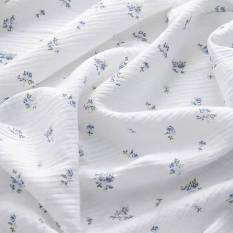 Peut inclure: Tissu en coton blanc avec un petit imprim&eacute; floral bleu. Le tissu a une surface textur&eacute;e, semblable &agrave; une gaufre.