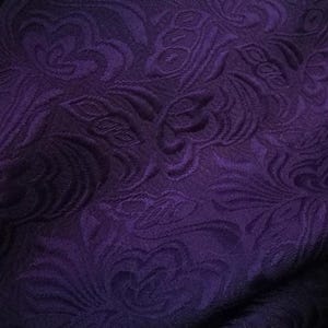May include: Purple fabric with a raised floral pattern. The fabric has a soft, textured feel.