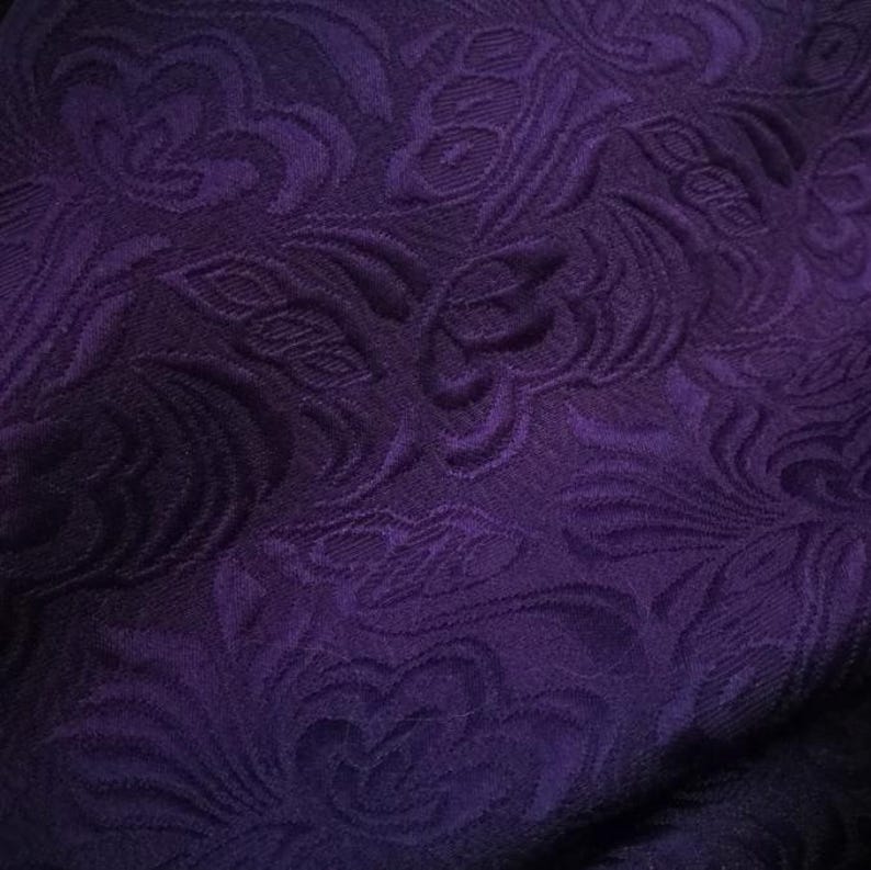 May include: Purple fabric with a raised floral pattern. The fabric has a soft, textured feel.