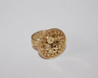 Könnte beinhalten: Ein goldener Ring mit einem großen, runden, verzierten Design. Der Ring ist aus filigraner Arbeit gefertigt und hat eine erhabene Mitte.
