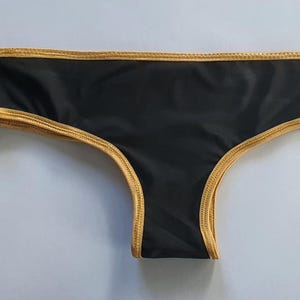 Dolda svarta stringtrosor med guldfärgat band, gjorda för transpersoner MTF/AMAB