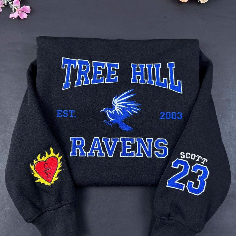 May include: Black sweatshirt with "TREE HILL RAVENS" in blue lettering. A blue raven graphic is centered below the text. The sleeve features a heart with "O/B" and the number "23" with "SCOTT".