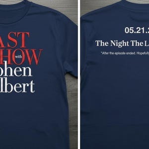 Puede incluir: Camiseta azul marino con el texto "The Last Show with Stephen Colbert" en rojo y blanco. La parte trasera muestra la fecha "05.21.2026" y la frase "The Night The Laughter Died".