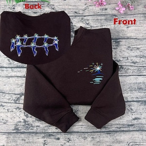 May include: A dark brown sweatshirt with embroidered designs. The front features a colourful sunburst design over a blue water line. The back has a circular design of blue figures holding hands. The sweatshirt has long sleeves.