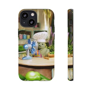 May include: A phone case featuring a whimsical kitchen scene. A green character in a chef's hat and apron stands behind a table with a blue fan. The background includes a wooden table, green peppers, and a bowl of food.