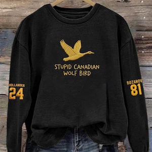 May include: Black sweatshirt with a gold embroidered flying duck and the text "STUPID CANADIAN WOLF BIRD". The left sleeve has "HOLLANDER 24" in gold, and the right sleeve has "ROZANOV 81".