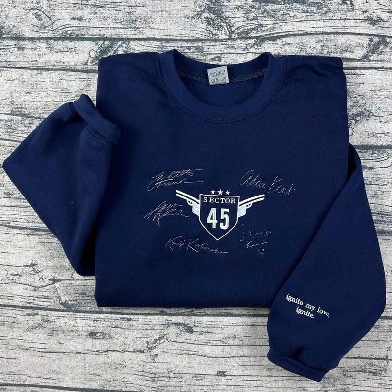 K&ouml;nnte beinhalten: Marineblaues Sweatshirt mit wei&szlig;er Stickerei. Es zeigt den Schriftzug "SECTOR 45" in einem Schild und Unterschriften. Der &Auml;rmel tr&auml;gt den Text "ignite my love, ignite".
