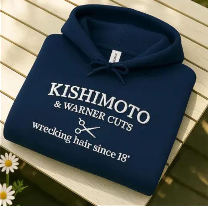 May include: A navy blue hooded sweatshirt with white embroidered text that reads "KISHIMOTO & WARNER CUTS wrecking hair since 18'" and a pair of scissors graphic. The sweatshirt has a drawstring hood.