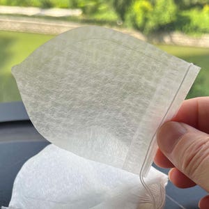 K&ouml;nnte beinhalten: Ein Stapel wei&szlig;er, halbtransparenter Teebeutel aus Vliesstoff. Jeder Beutel hat eine abgerundete, blatt&auml;hnliche Form mit einer hei&szlig;versiegelten Kante und einer d&uuml;nnen wei&szlig;en Schnur an der oberen Ecke zur einfachen Handhabung beim Aufbr&uuml;hen.
