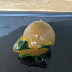 以下が含まれることがあります： 茶色と金色の丸みを帯びた質感の甲羅を持つセラミック製のカメの置物。カメの頭と足は対照的な緑と黄色です。置物は暗い表面にあります。