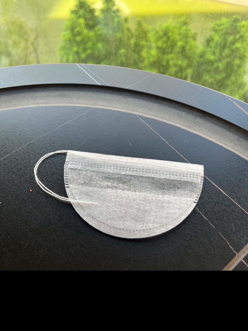 K&ouml;nnte beinhalten: Ein halbkreisf&ouml;rmiger wei&szlig;er Teebeutel aus d&uuml;nnem, por&ouml;sem Papiermaterial. Der Teebeutel hat eine gerade Oberkante mit einer gen&auml;hten Naht und eine abgerundete Unterkante. Ein d&uuml;nner wei&szlig;er Faden ist an der linken Seite befestigt.