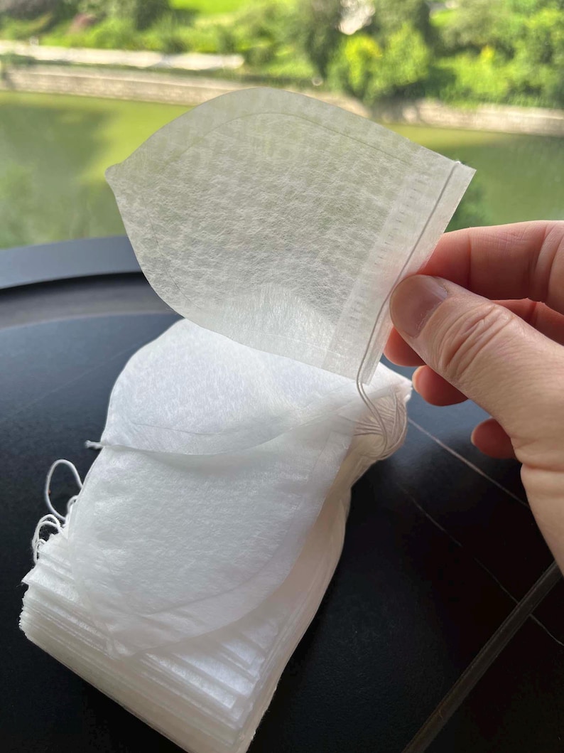 K&ouml;nnte beinhalten: Ein Stapel wei&szlig;er, halbtransparenter Teebeutel aus Vliesstoff. Jeder Beutel hat eine abgerundete, blatt&auml;hnliche Form mit einer hei&szlig;versiegelten Kante und einer d&uuml;nnen wei&szlig;en Schnur an der oberen Ecke zur einfachen Handhabung beim Aufbr&uuml;hen.