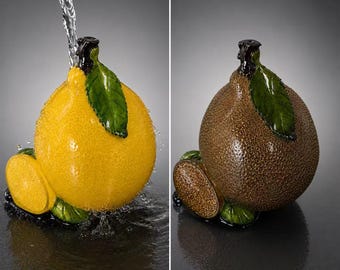 May include: A ceramic fruit-shaped vessel with a textured surface, featuring a green leaf and a small slice attached at the base. One version is bright yellow, while the other is a dark brown, both shown with water pouring over the top.