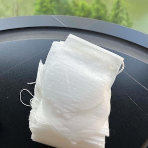 K&ouml;nnte beinhalten: Ein Stapel rechteckiger wei&szlig;er Teebeutel aus d&uuml;nnem, halbtransparentem Papier. Jeder Teebeutel verf&uuml;gt &uuml;ber eine hei&szlig;versiegelte Oberkante und eine d&uuml;nne wei&szlig;e Schnur an der Seite, die zum Aufbr&uuml;hen von losem Tee in hei&szlig;em Wasser dient.