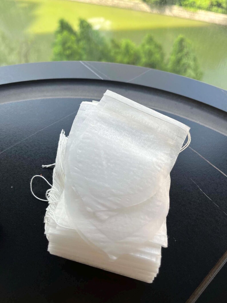 K&ouml;nnte beinhalten: Ein Stapel rechteckiger wei&szlig;er Teebeutel aus d&uuml;nnem, halbtransparentem Papier. Jeder Teebeutel verf&uuml;gt &uuml;ber eine hei&szlig;versiegelte Oberkante und eine d&uuml;nne wei&szlig;e Schnur an der Seite, die zum Aufbr&uuml;hen von losem Tee in hei&szlig;em Wasser dient.