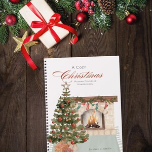 May include: A spiral-bound book titled "A Cozy Christmas" with a watercolor illustration of a Christmas tree and fireplace. The book is surrounded by Christmas decorations, including a wrapped gift, ornaments, and greenery.