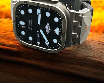 May include: A black and silver wristwatch with a black face and white hour markers. The watch has a black rubber strap and a silver metal band. The watch face displays the text "SUBMERGE" and "Sat 17".
