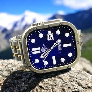 Puede incluir: Un reloj de pulsera de acero inoxidable con esfera cuadrada y azul. El reloj tiene marcadores de hora y agujas blancas, una ventana de fecha y una correa de metal. El reloj está sobre un fondo borroso de montañas y cielo.
