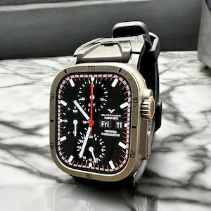 Puede incluir: Primer plano de un reloj inteligente con esfera negra y caja plateada. La esfera muestra el texto "BLACKHAWK FLIGHT DECK" y "Fri 11". El reloj tiene una correa negra y una esfera roja y blanca.