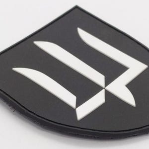 Op de afbeelding: Zwarte patch met een wit gestileerd letter W-ontwerp. De patch is gemaakt van duurzaam materiaal en heeft een gestikte rand.