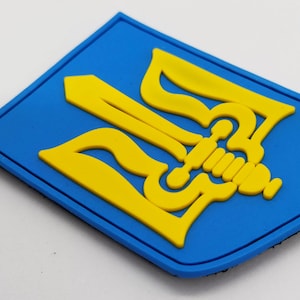Könnte beinhalten: Ein blauer und gelber gestickter Aufnäher mit dem ukrainischen Wappen, einem Dreizack.
