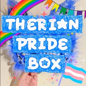May include: A blue faux fur item featuring a graphic overlay with the text THERIAN PRIDE BOX in white letters. The image includes a rainbow arch, colorful triangular bunting, small star icons, and a pink, white, and blue striped flag.