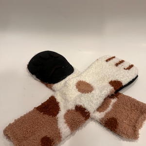 May include: A pair of cozy socks with a paw print design. The socks are white with brown spots and a brown cuff. The soles are black.