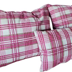 May include: Four rectangular pillows with a plaid pattern in shades of pink, white, and brown. The pillows are arranged in a group, with varying sizes. The fabric has a soft, textured appearance.