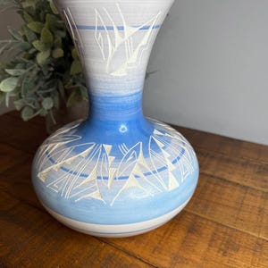 Peut inclure: Un vase en céramique bleu et blanc avec une base large et un col étroit. Le vase présente un motif géométrique blanc sur fond bleu.