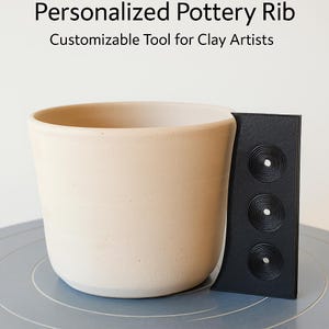 Puede incluir: Una herramienta de costilla de cerámica negra con tres patrones circulares de diferentes tamaños. La herramienta se utiliza para crear textura en la arcilla.