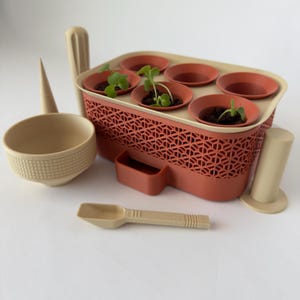 May include: A beige and terracotta-colored seed starting kit with six small pots containing soil and seedlings. The kit includes a scoop, a funnel, a bowl, and a cylindrical support. The terracotta-colored container has a geometric pattern.