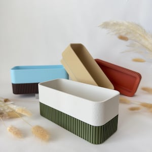 May include: Rectangular storage containers in various colors: white and green, light blue and brown, tan, and red. The containers have a textured surface and a ribbed design on the lower half. The containers are empty and arranged on a white surface.