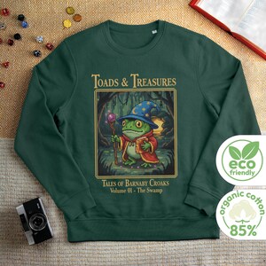 May include: Dark green sweatshirt with a cartoon frog wizard design and the text "TOADS & TREASURES". The frog wears a blue wizard hat and red robe, holding a staff and book. Made from 85% organic cotton.
