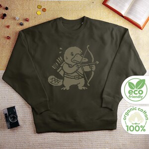 May include: An olive green long-sleeve sweatshirt featuring a pixelated graphic of a platypus dressed as an archer, holding a bow and arrow with a quiver on its back. The design is rendered in a lighter shade of green against the dark fabric.